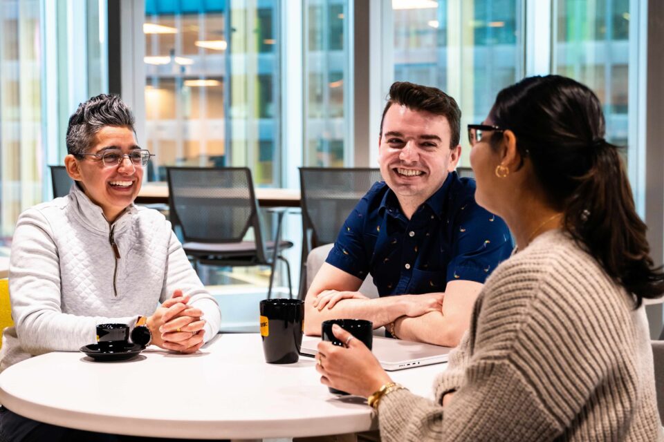 Three people seated around a table in a office setting, engaged in a discussion.